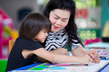 Obraz premium Mom gave her daughter some advice for making crafts. Doing activities together in the family. Girl happily made art. Child smiles sweetly. Kid wearing black shirts aged 5-6 years. Homework. Stay home.