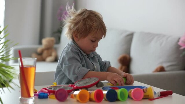 Cute blond child,  sweet boy, playing with play doh modeline at home, making different objects
