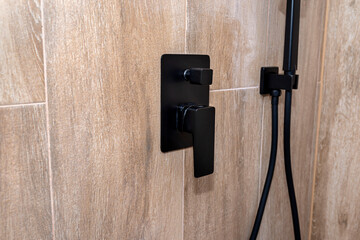 Black, matt metal shower faucet protruding from the tiled wall, imitating wood.