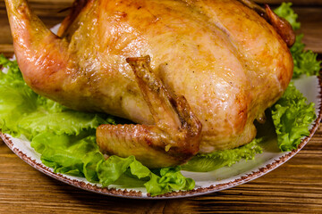 Plate with roasted whole chicken and lettuce leaves on a wooden table
