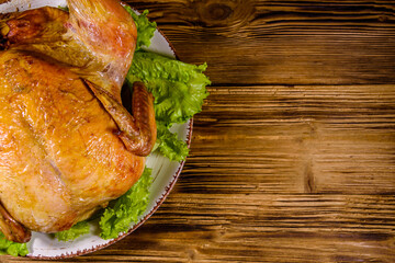 Plate with roasted whole chicken and lettuce leaves on a wooden table. Top view