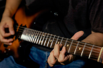 Fototapeta na wymiar Closeup of male guitarist's hand and finger during playing guitar and a hand push on string on the guitar neck for chord while perform electric guitar lead solo. Rock l practice.