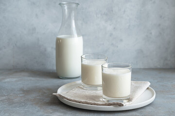 Two glasses and a bottle of fresh milk drink on a gray background.