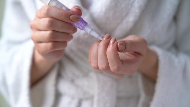 Closeup female hands are holding little bottle with nourishing cuticle oil. Young woman girl is smearing her nails, making herself hygienic manicure. Personal hygiene and care products concept.