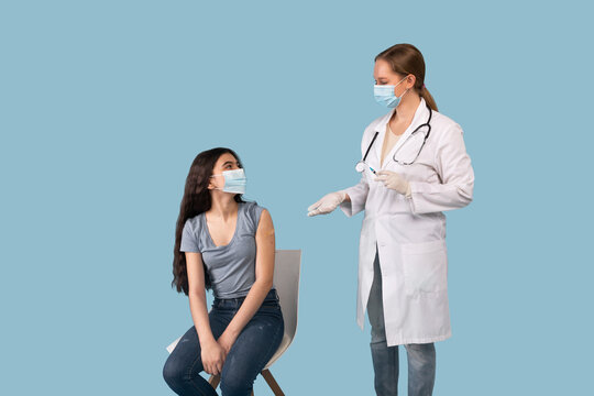 Young Female Doctor Talking To Teen Patient After Giving Her Shot Of Coronavirus Vaccine Over Blue Studio Background