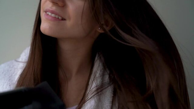 Closeup of female hands are holding modern hairdryer. Young smiling woman girl is drying hair after washing, doing hairstyle. Tools and devices for styling. Personal hygiene and care concept.