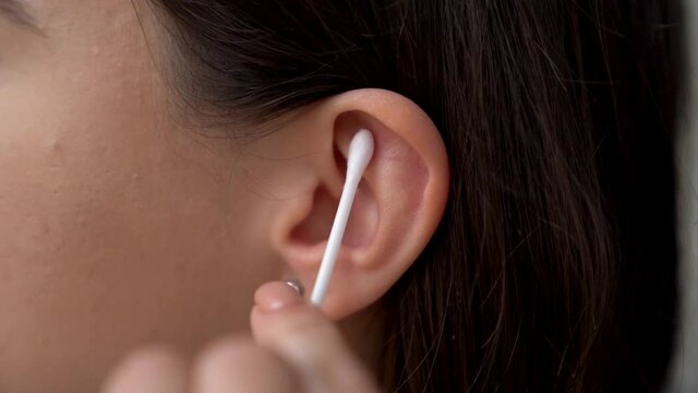 Young woman is holding in hand disposable cotton bud, swab, stick. Girl is cleaning, washing her auricle. Personal hygiene and care product concept. Prevention of ear diseases. Earwax removal.