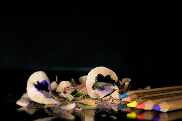Colored pastel pencils and pencil shavings on a black background