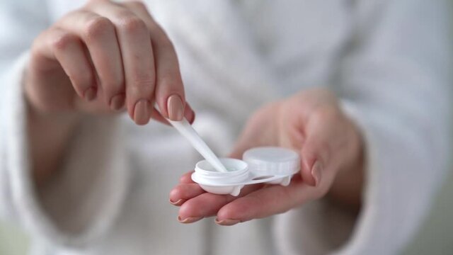 Closeup female hands are holding plastic container for contact lenses. Woman is washing soft optical lens in cleaning liquid, preparing to put in eye. Vision correction of myopia, hyperopia concept.