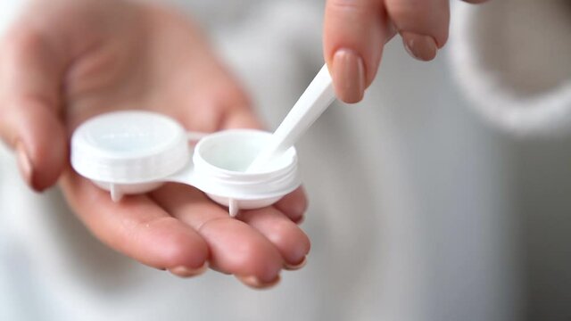 Closeup female hands are holding plastic container for contact lenses. Woman is washing soft optical lens in cleaning liquid, preparing to put in eye. Vision correction of myopia, hyperopia concept.