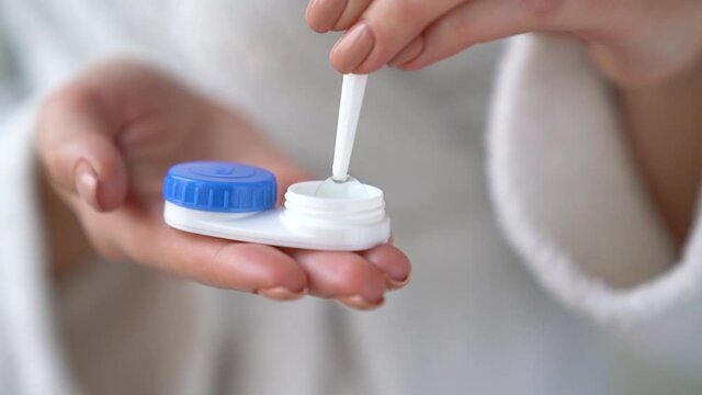 Closeup female hands are holding plastic container for contact lenses. Woman is washing soft optical lens in cleaning liquid, preparing to put in eye. Vision correction of myopia, hyperopia concept.