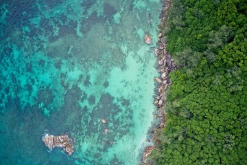 rone field of view of rocky coastline with cliffs meeting sea of turquoise blue Praslin Seychelles.