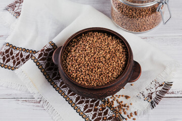 Bowl of dry raw buckwheat groats on a white wooden background