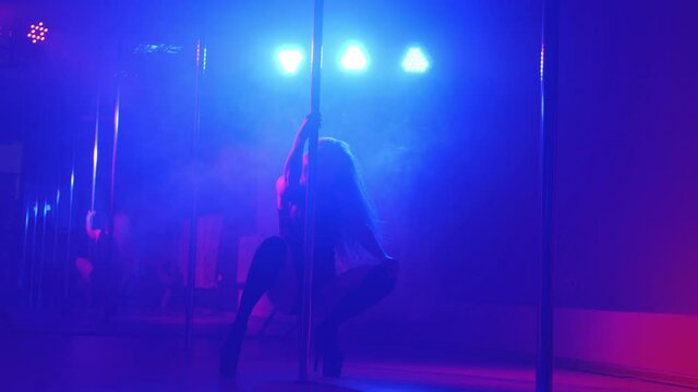 Pole dance. Young slender sexy woman dancing on a pole in the interior of a nightclub with light and smoke.