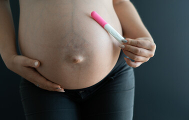 Pregnant woman with a big belly holding a pregnancy test.