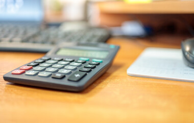 calculator is on the table against background of the keyboard and mouse, background is blurred