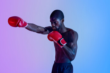 Professional boxing concept. Muscular African American boxer in red gloves making punch in neon lighting