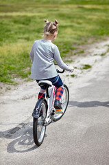 Little girl biking on sunny summer day in city park. Children learning to drive a bicycle on a driveway outside