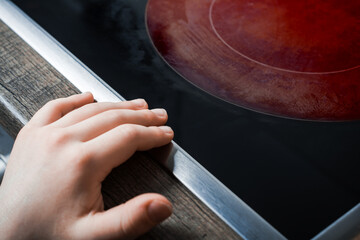 Hand Of A Child Reaches Active Hotplate Of A Kitchen Glass-Ceramic Stove - Prevent Child Hazard...