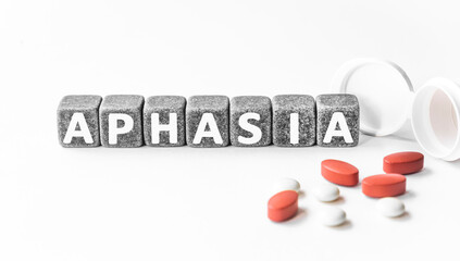 word APHASIA is made of stone cubes on a white background with pills. medical concept of treatment, prevention and side effects. Difficulty speaking or comprehending language, stroke