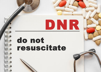 Page in notebook with DNR on white background with stethoscope and group of pill. Medical concept. Term and abbreviation. do not resuscitate