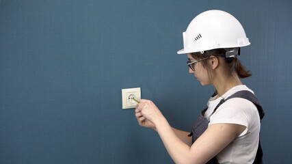 An electrician repairs an outlet in the house. A woman in special clothing and a helmet installs an...