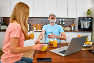 Happy married couple have breakfast and have fun using laptop in the kitchen. Healthy lifestyle concept.