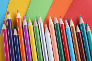 Many multi colored pencils lying on bright colorful background