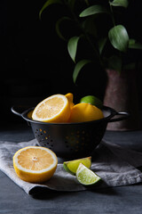 juicy lemons and limes in a black bowl on a gray table. Dark and mood concept