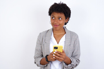 African American businesswoman with curly bushy hair wears  formal clothes over white background holds telephone hands reads good youth news look empty space advert