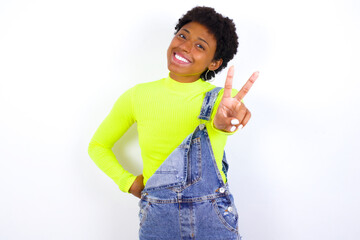 young African American woman with short hair wearing denim overall against white wall directs fingers at camera selects someone. I recommend you. Best choice