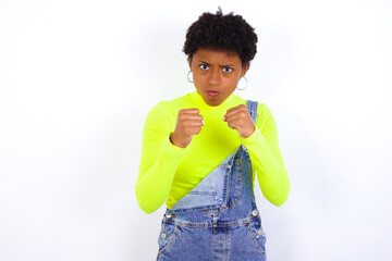 Displeased annoyed young African American woman with short hair clenches fists, gestures pissed, ready to revenge, looks with aggression at camera stands full of hate, being pressured