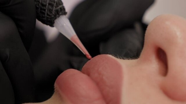 Close-up of the process of applying permanent makeup to the lips.