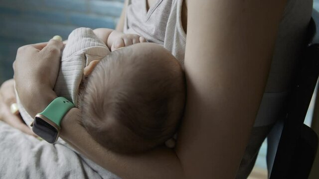 Young woman feeds breast milk to her newborn baby close-up.