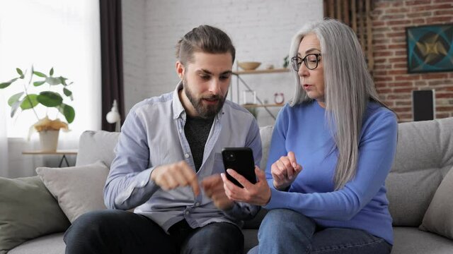 Adult son teaching his senior mother to use smartphone mobile apps. Mom does not understand expalanations, son feeling nervously. Family and generations conflicts, misunderstanding.