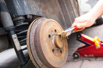 Cleaning the car's brake drum from rust with a wire brush