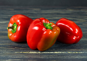 Three bulgarian red peppers in a close-up plan on a dark wooden background.