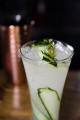white cocktail with cucumber and ice in a bar at night
