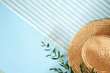Vacation & travel concept, top view, flat lay, beach hat and green myrtle with copy space diagonally. Straw hat and a branch of myrtle on a blue background with white stripes diagonally.