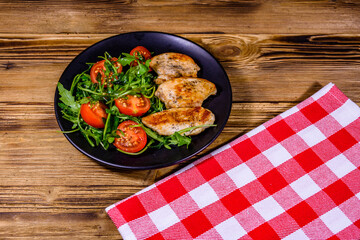 Roasted chicken breasts and salad with arugula and cherry tomatoes in a black plate