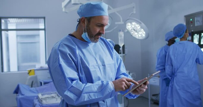 Portrait of caucasian male surgeon standing in operating theatre using tablet