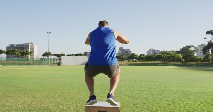 Back view of fit caucasian man exercising outdoors jumping on box