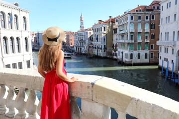 Fototapeta na wymiar Tourism in Venice. Back view of beautiful young woman in red dress enjoying view of Grand Canal from Rialto Bridge in Venice, Italy.
