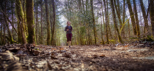 Caucasian Woman Trail Running in the Green Forest surrounded by beautiful trees. Taken in Squamish, British Columbia, Canada.