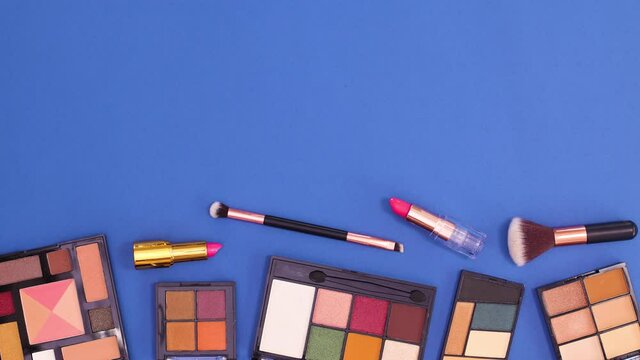 Eye shadow palettes and brushes appear on bottom of dark blue background. Stop motion flat lay