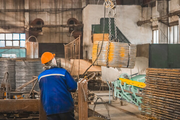 Worker in a reinforcement workshop in a helmet controls equipment for moving metal structures