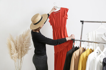 Beautiful young woman near rack with clothes holding long terracotta dress.