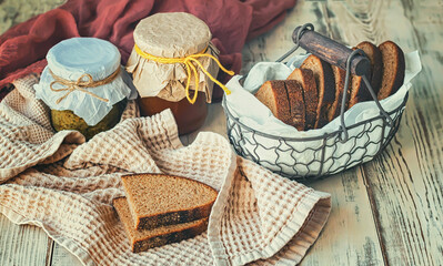 Vintage basket with bread, fruit jam and pesto sauce on a wooden background, selective focus.