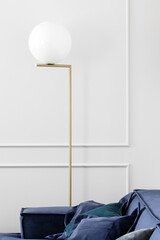 Round gold and white lamp in interior with blue lounge sofa and white wall