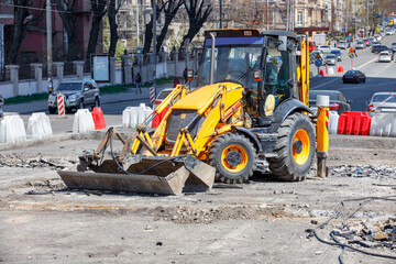 Fototapeta premium A compact tractor with pavement repair attachments stands on a work platform against the backdrop of a city street.